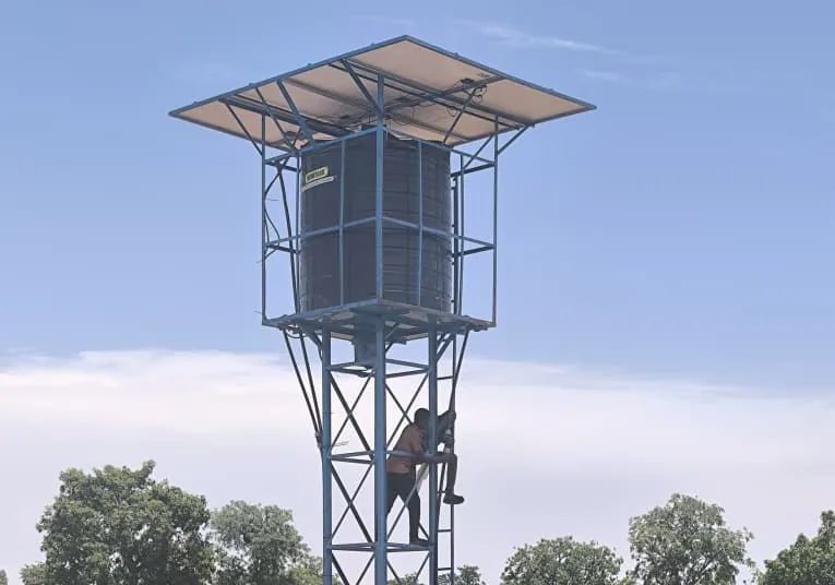 Château d’eau métallique alimenté par panneaux solaires, au-dessus d’un forage